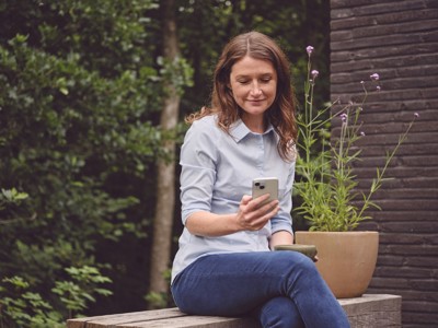 Kvinde i en have med telefon i hånden.